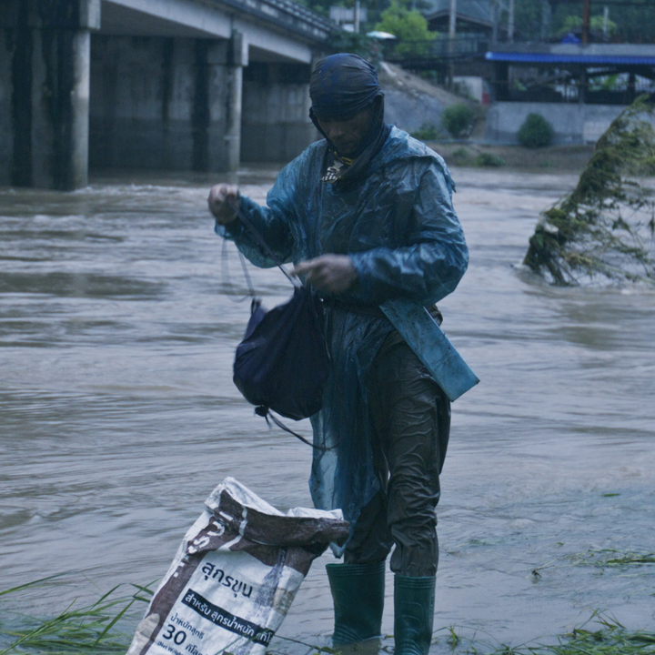 Ein durchnässter Fischer steht am Rande eines Flüssel, der Hochwasser führt.