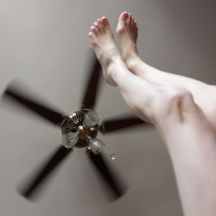 Ein Standbild aus Moyra Daveys Film "My Saints" (2014). Nach oben ausgestreckte, bloße Beine, dahinter ein Deckenventilator.
